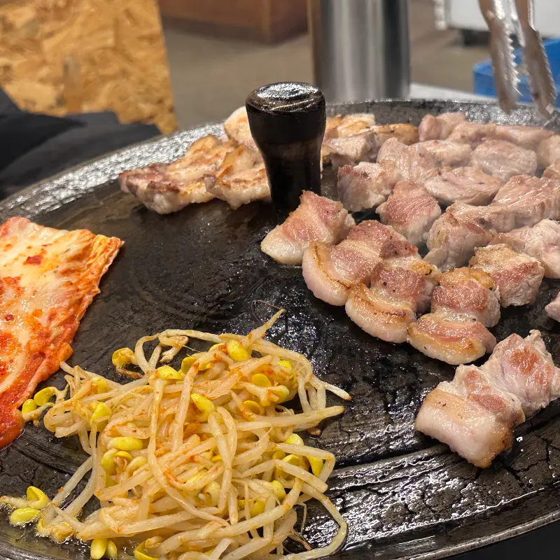 솥뚜껑에 삼겹살, 김치, 콩나물이 함께 구워지는 모습