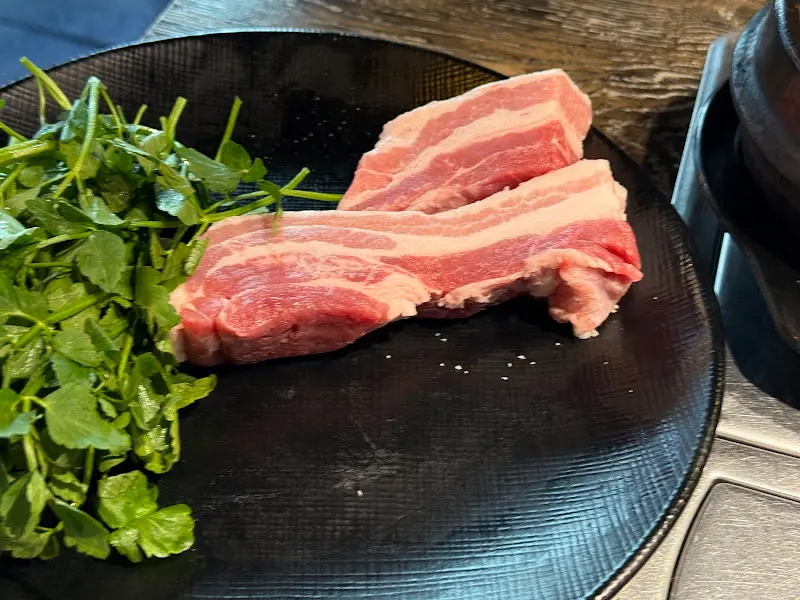 접시에 담긴 숙성 삼겹살과 미나리