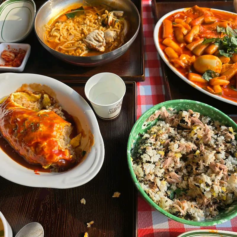 오므라이스, 라면, 떡볶이, 참치주먹밥이 차려진 테이블