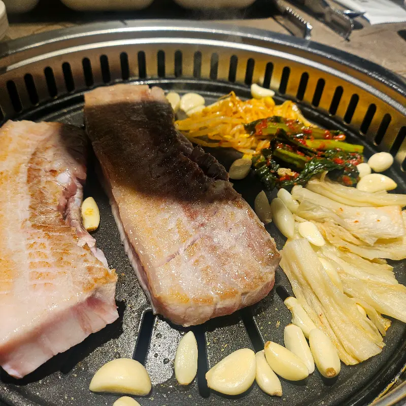 불판 가득 채워진 삼겹살과 김치, 마늘