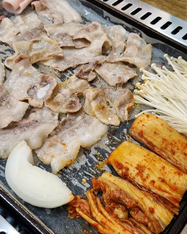 불판 위에서 익어가는 삼겹살과 김치, 버섯