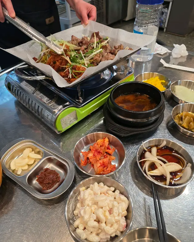 테이블 위 작은 휴대용 버너 위에 불고기가 올려져 있고, 주위에 다양한 밑반찬 그릇들이 놓여있다.