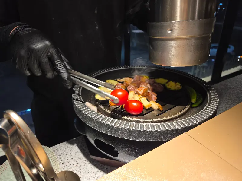 직원이 집게를 이용하여 불판 위의 고기를 굽고 있는 모습