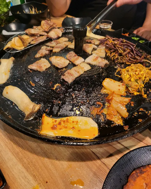 솥뚜껑 위에서 삼겹살과 김치, 콩나물 등이 맛있게 구워지는 모습