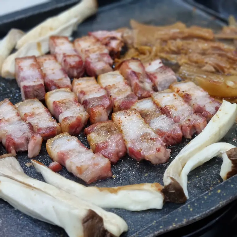 불판 위에서 맛있게 익어가는 삼겹살과 버섯