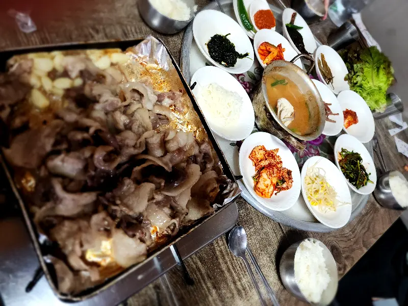 다채로운 반찬과 꽃게 된장찌개, 냉동 삼겹살이 놓인 푸짐한 한 상