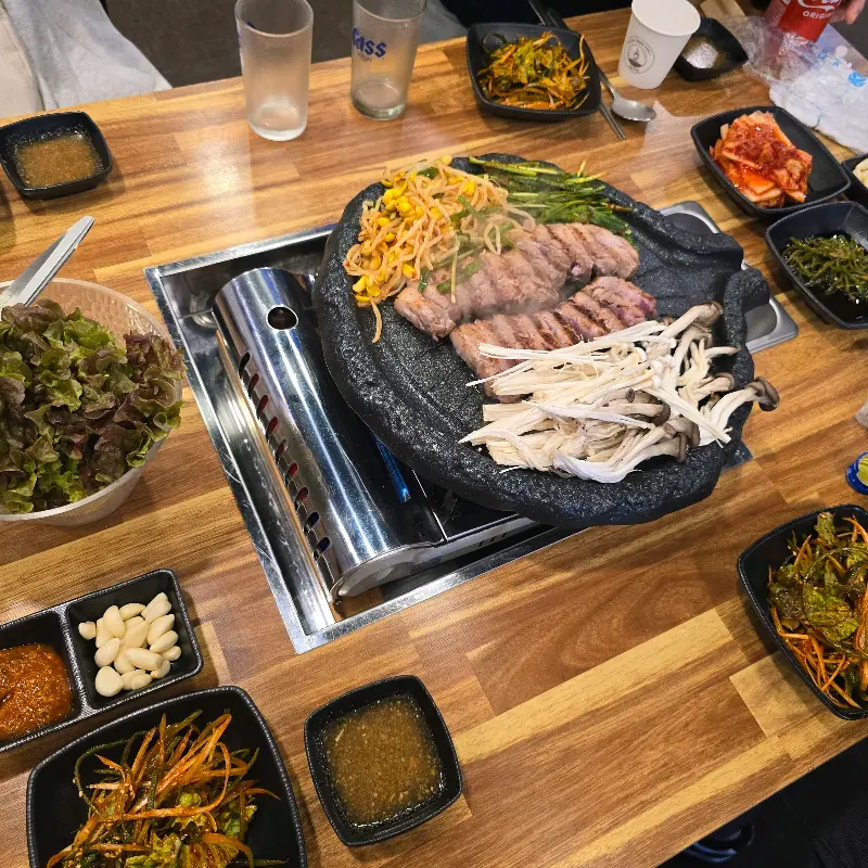 솥뚜껑에 삼겹살과 다양한 구워먹는 재료들이 함께 올려져 있는 모습