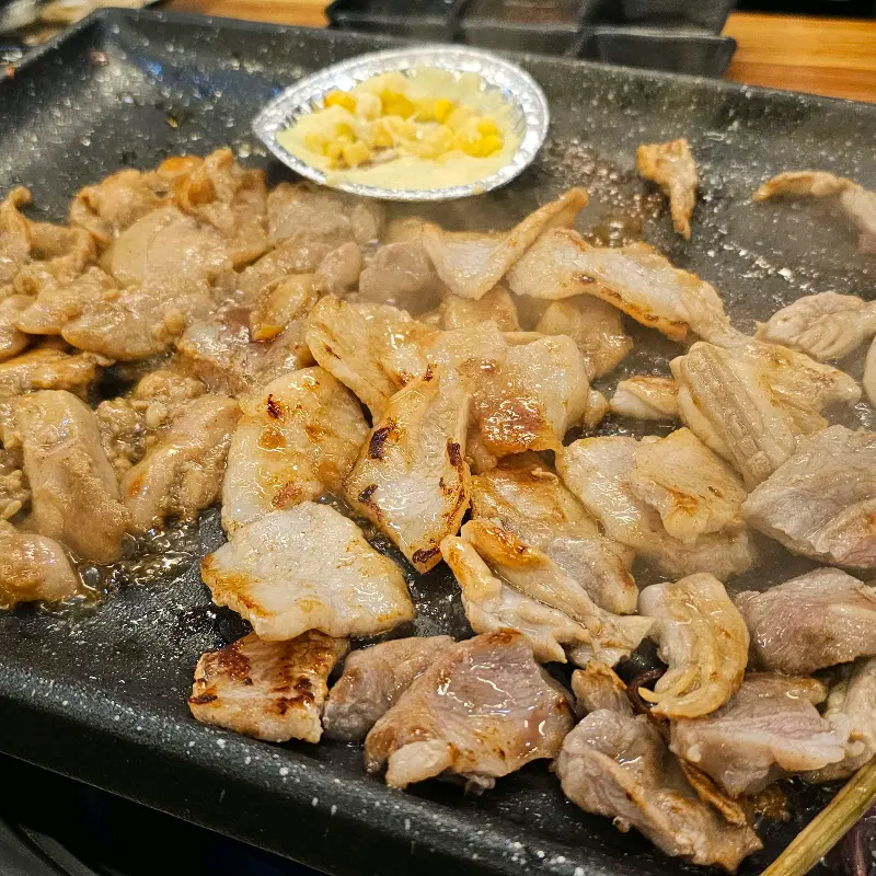 불판 위에서 익어가는 삼겹살과 콘치즈