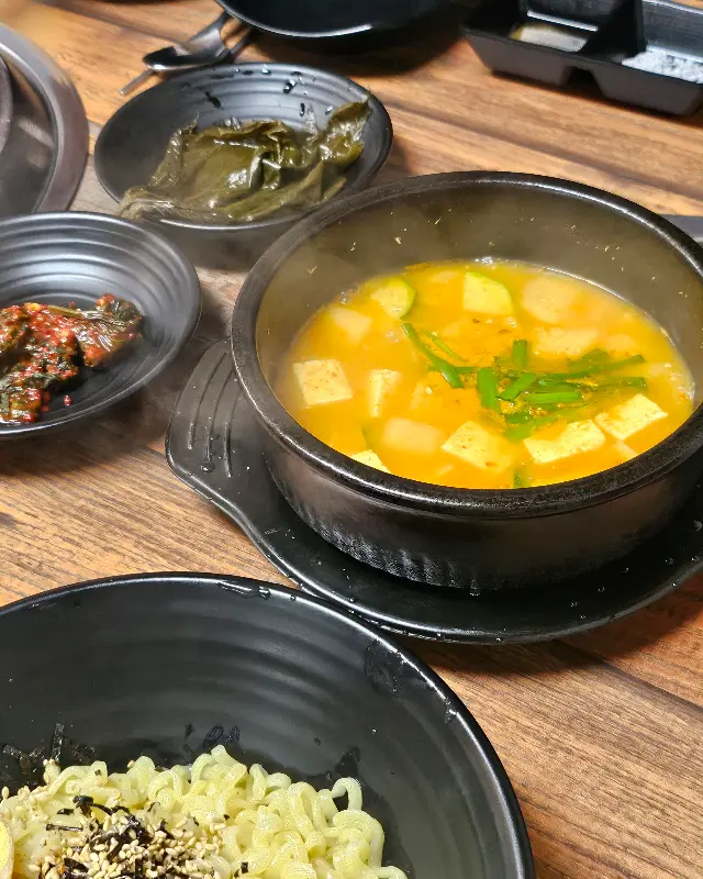 잘 익은 고기와 함께 짜파게티, 된장찌개 등이 놓여 있는 테이블 모습