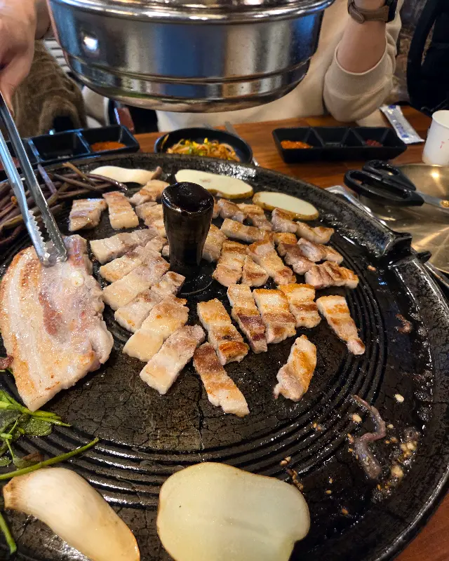 솥뚜껑에 김치와 콩나물을 올려 굽는 모습