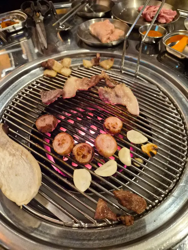 연탄불 위에서 삼겹살, 뒷고기, 버섯, 마늘이 함께 구워지는 모습