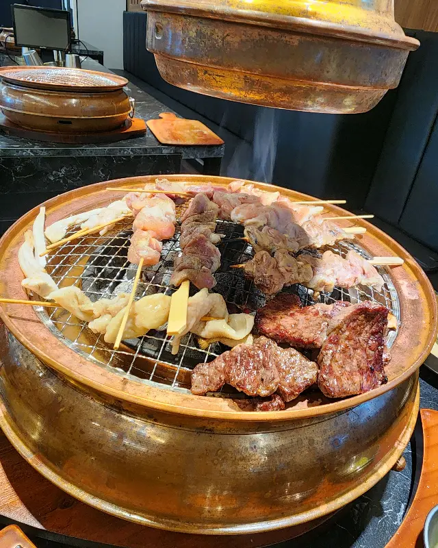 화로 위 석쇠에 여러 종류의 꼬치와 고기가 함께 구워지고 있는 모습