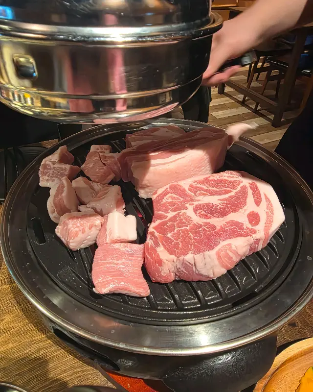 숯불 위에서 익어가는 두툼한 돼지고기 목살과 삼겹살