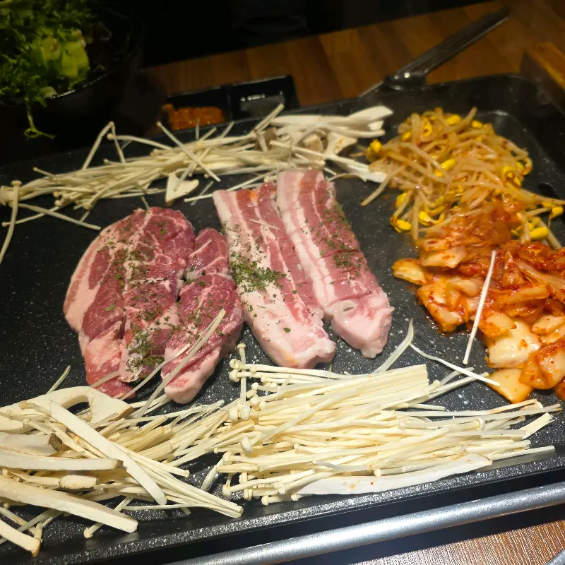 불판 위에 올려진 삼겹살과 곁들임 채소들