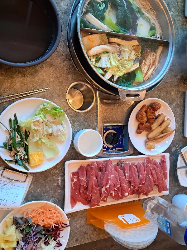 샤브샤브 냄비와 고기, 곁들임 채소들이 테이블 위에 놓여 있는 모습
