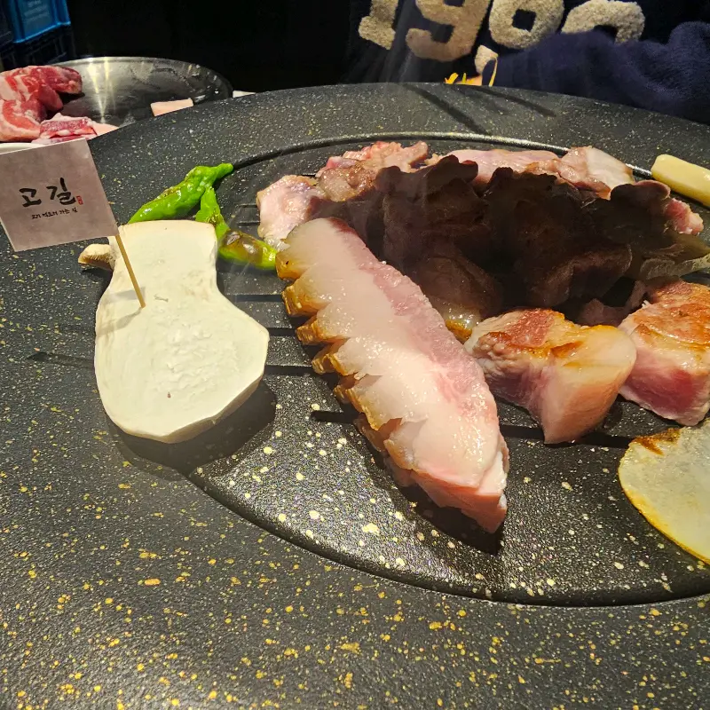 잘 구워진 고기와 곁들여 먹기 좋은 반찬들이 테이블 위에 놓여 있다.