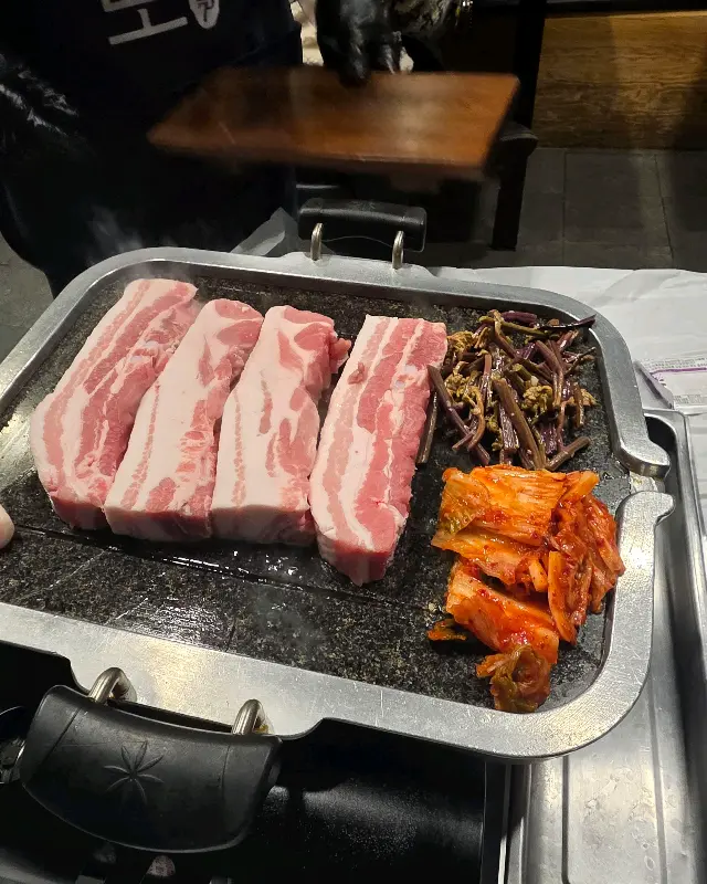 불판 위에 올려진 삼겹살과 김치, 고사리