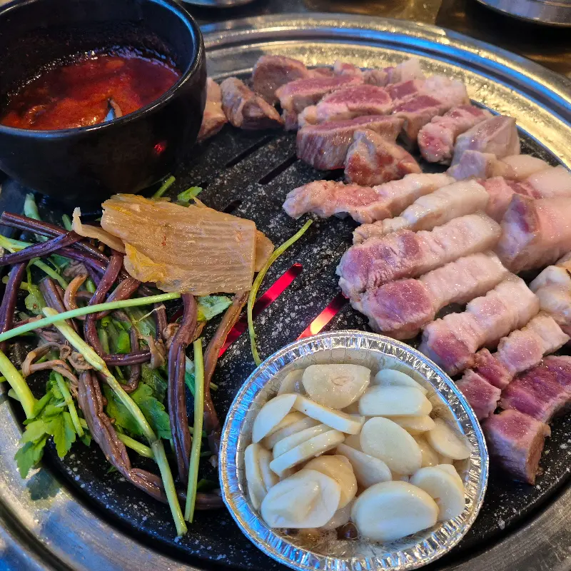 불판 위에서 지글거리는 흑돼지 목살, 멜젓, 미나리, 마늘