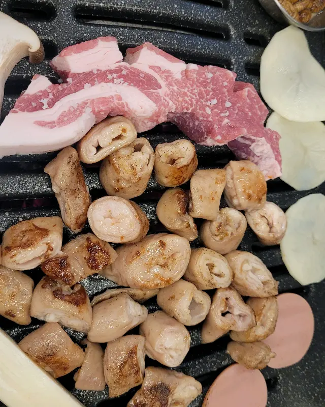 불판 위에서 막창과 함께 구워지는 버섯, 떡, 슬라이스 햄