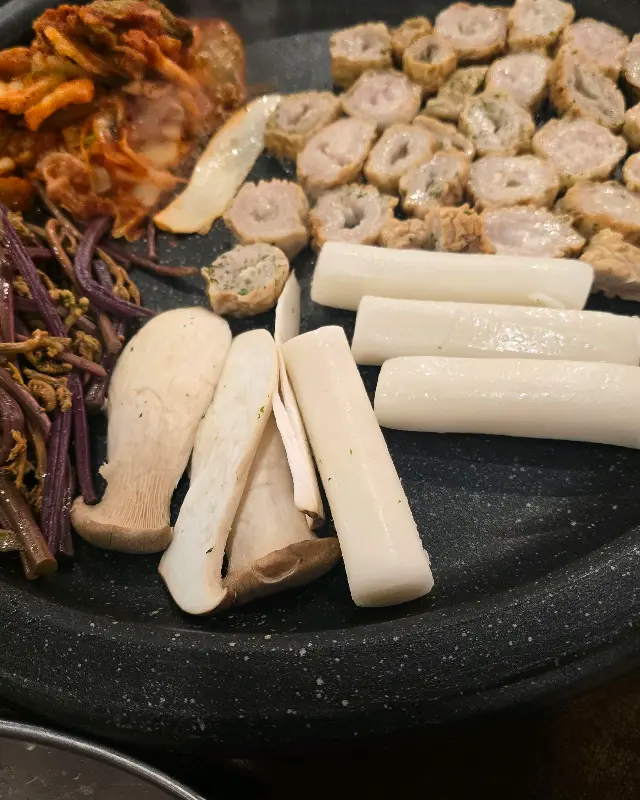 불판 위에 함께 구워지고 있는 막창, 버섯, 떡, 김치