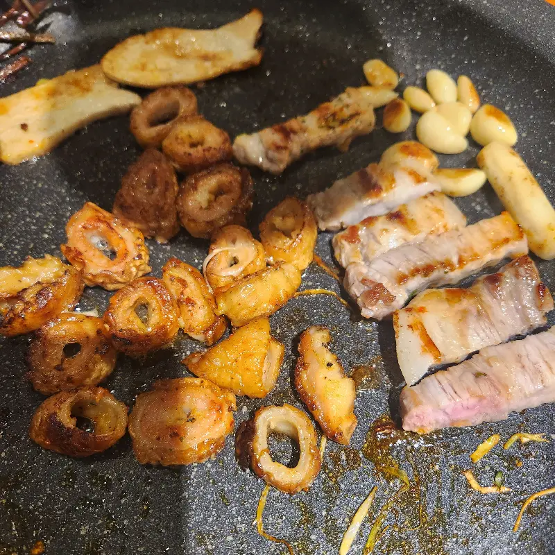 노릇하게 구워진 막창, 삼겹살, 마늘, 떡