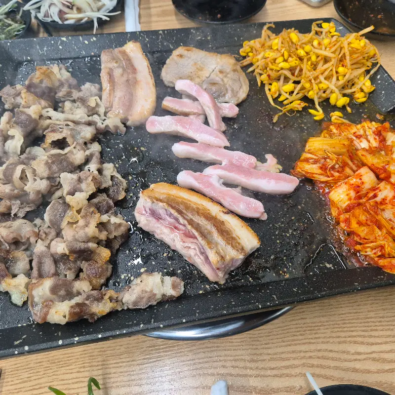 불판 가득 채워진 우삼겹, 삼겹살, 김치, 콩나물, 버섯