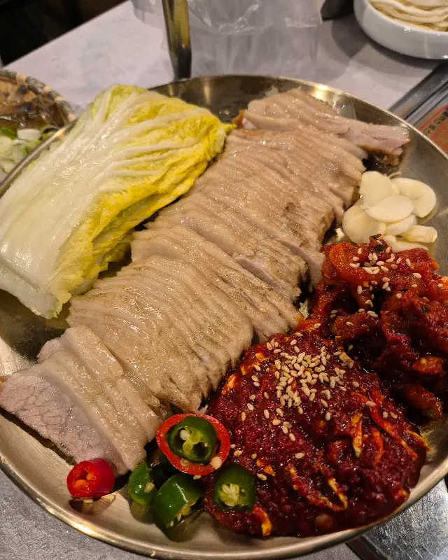 윤기가 흐르는 가브리살 보쌈과 신선한 배추, 매콤한 김치 속이 한 접시에 담겨 있다.