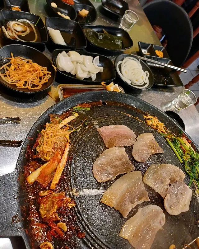 솥뚜껑에 삼겹살, 김치, 콩나물 등이 맛있게 구워진 모습