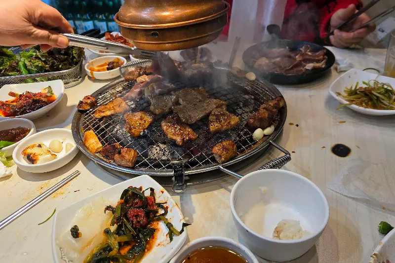 숯불 위에서 익어가는 돼지갈비와 다양한 반찬들