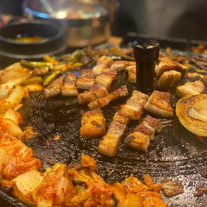 솥뚜껑에 삼겹살과 김치를 함께 구워 먹는 모습