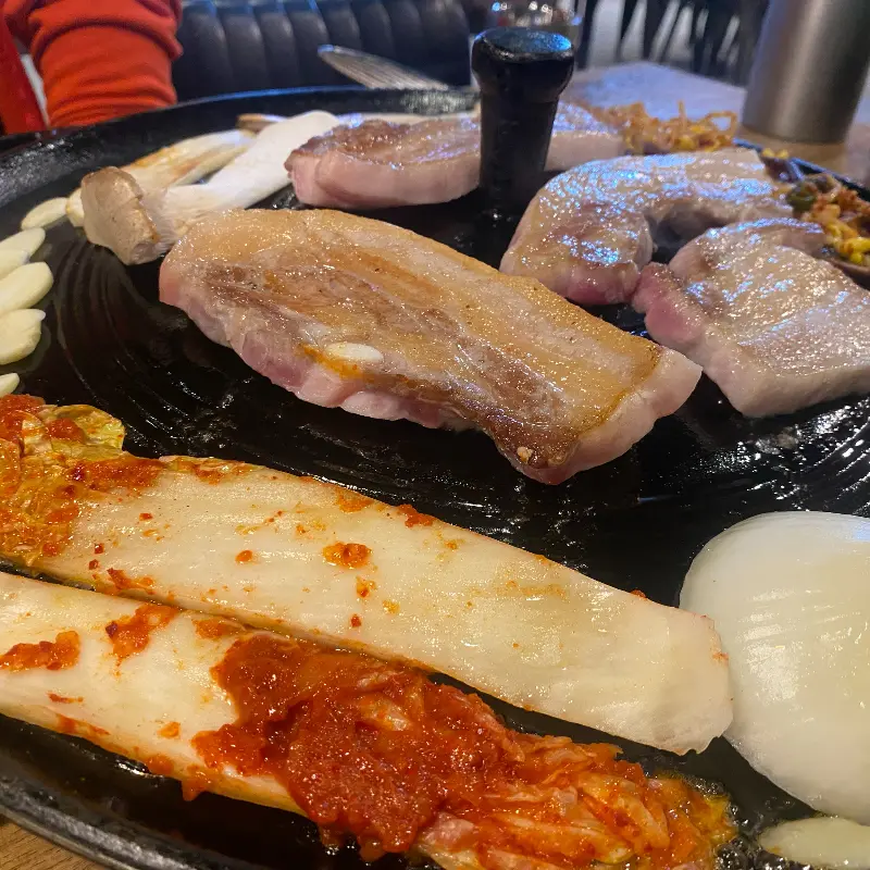 솥뚜껑 위에 삼겹살과 다양한 곁들임 메뉴들이 놓여 있는 모습