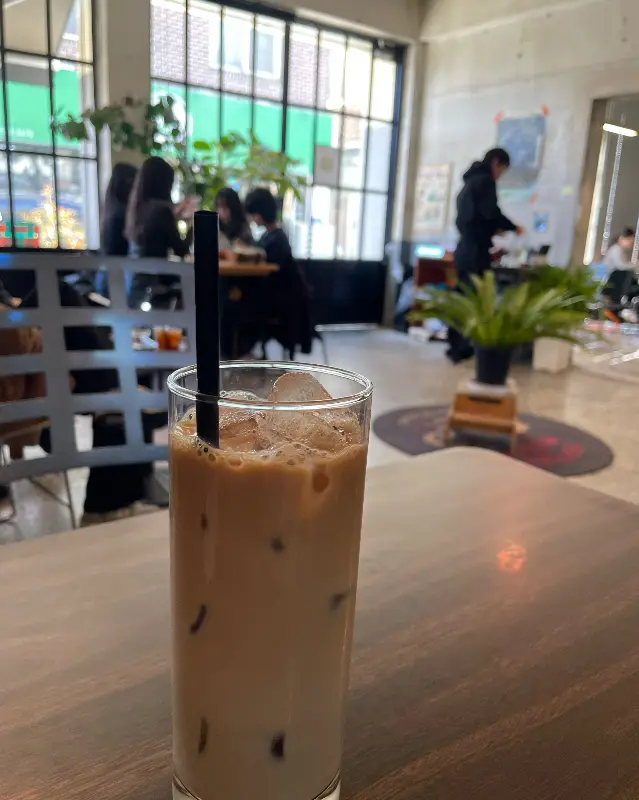 카페 내부의 테이블 위에 놓인 라이드 커피. 유리잔에 담겨 있으며, 얼음이 들어 있다. 배경에는 사람들이 앉아 있는 모습이 보인다.