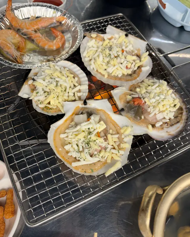 불판 위에서 치즈를 올려 구워지고 있는 가리비 사진