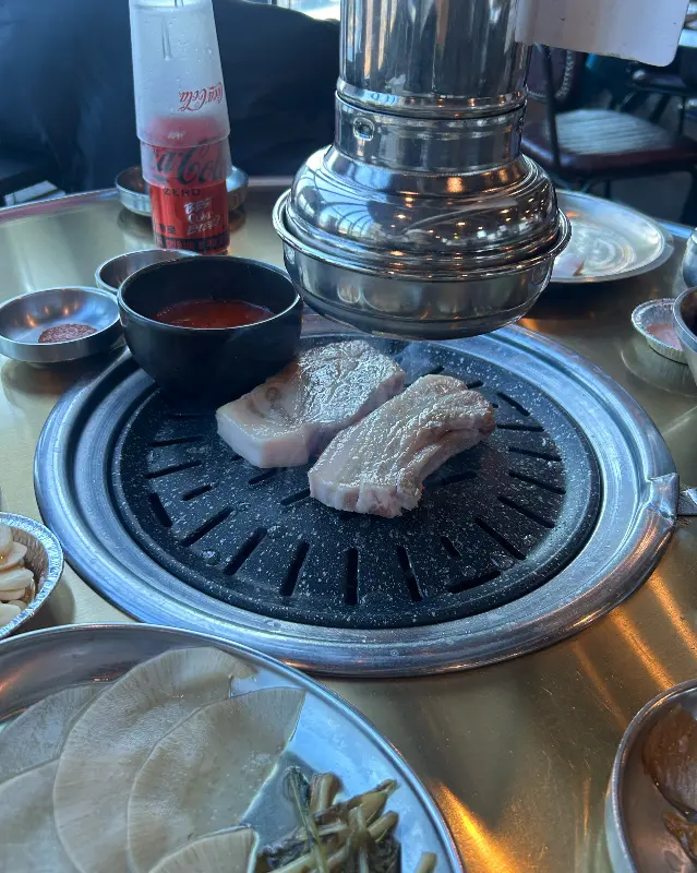 불판 위에서 익어가는 흑돼지 오겹살과 함께 보이는 은색 환풍구