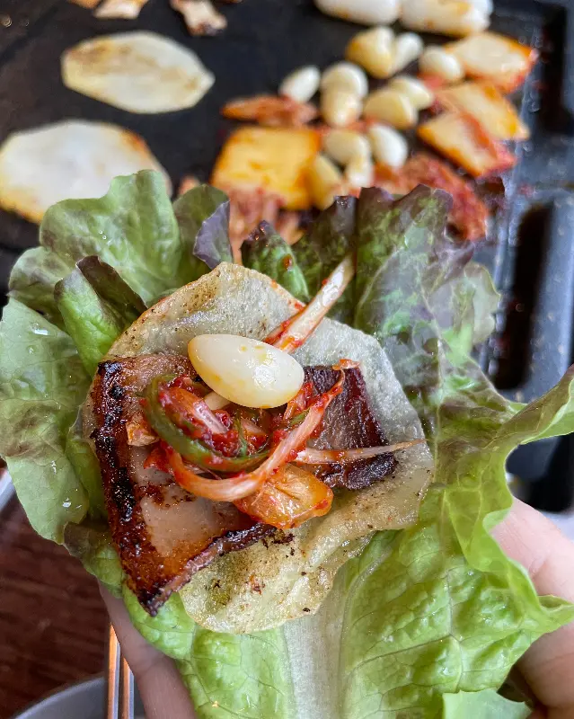 쌈 위에 냉삼과 마늘, 김치를 올려 먹음직스럽게 쌈을 싼 모습