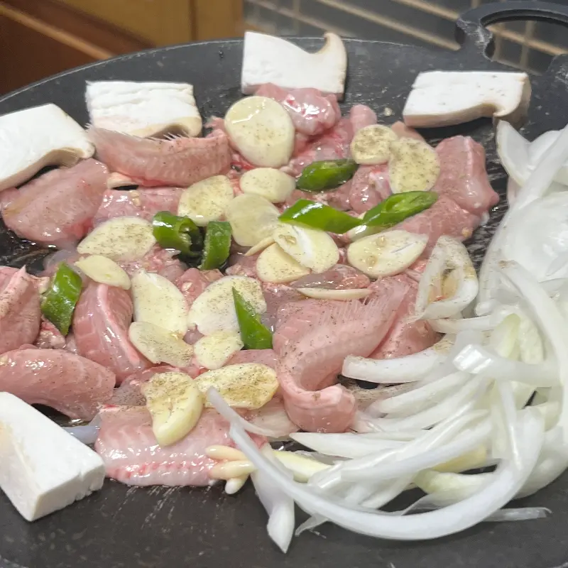 불판 위에 곰장어, 마늘, 양파, 버섯 등이 함께 구워지고 있는 모습