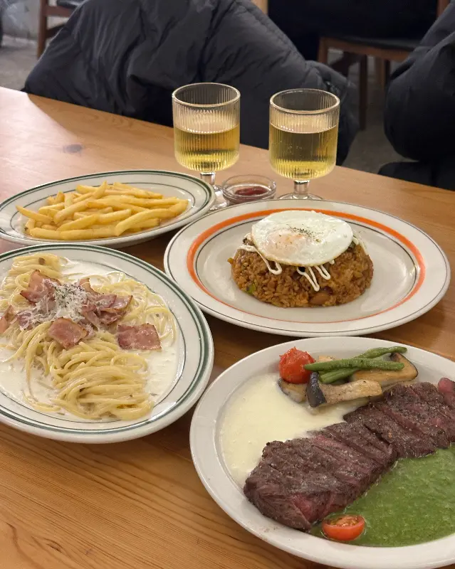 스테이크, 파스타, 필라프, 감자튀김과 음료가 차려진 테이블