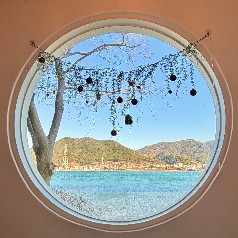 둥근 창문 너머로 보이는 푸른 바다와 섬의 풍경