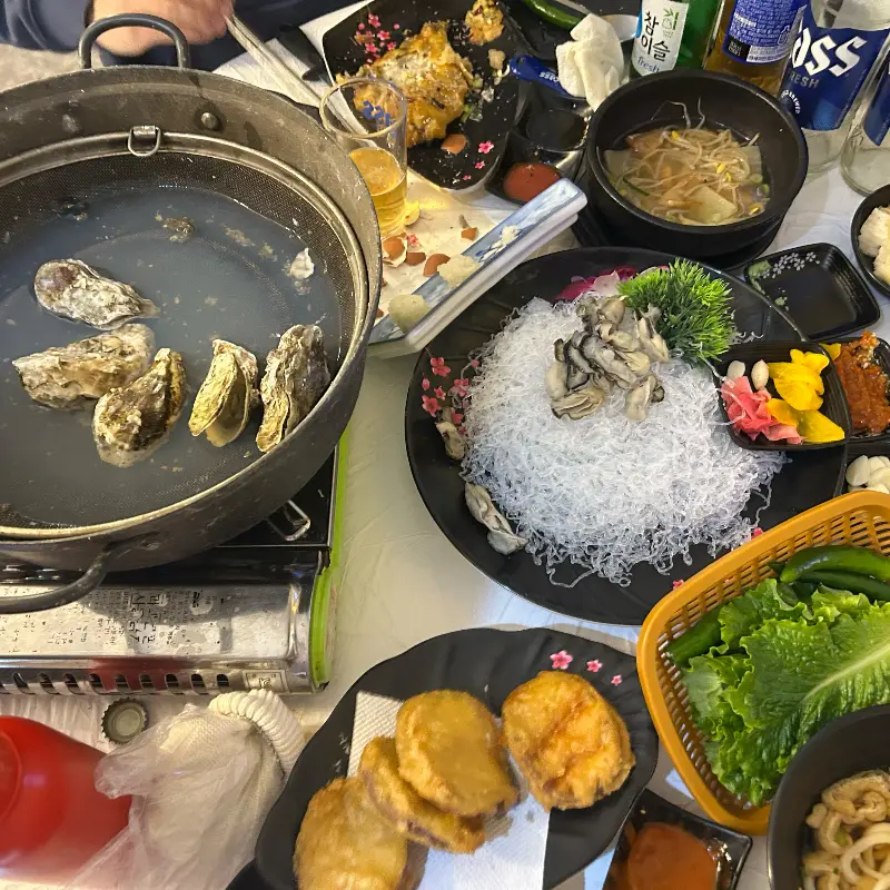 굴찜이 담긴 냄비와 다양한 스끼다시가 테이블 위에 푸짐하게 차려진 모습