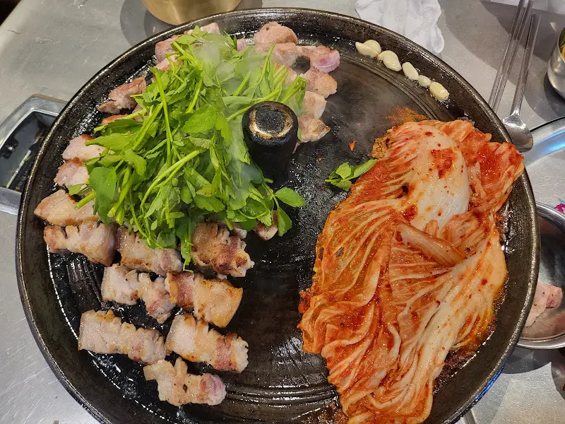 삼겹살, 김치, 미나리가 솥뚜껑에 함께 구워져 있는 모습