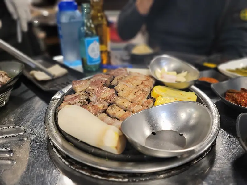 불판 위에 오겹살, 에린기 버섯, 떡 등이 함께 구워지고 있다.