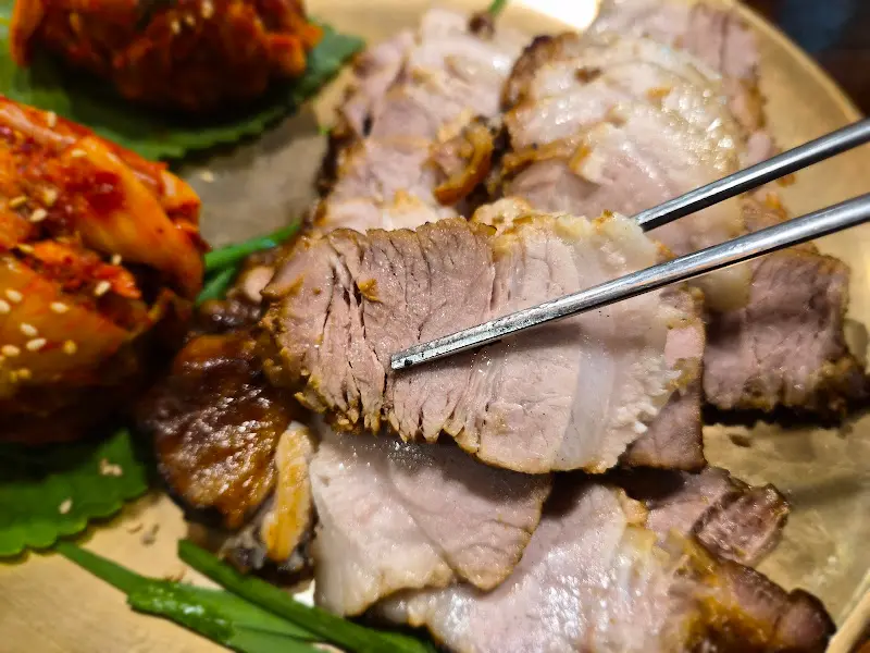 보쌈 한 점을 젓가락으로 들어올려 김치와 함께 먹으려는 모습