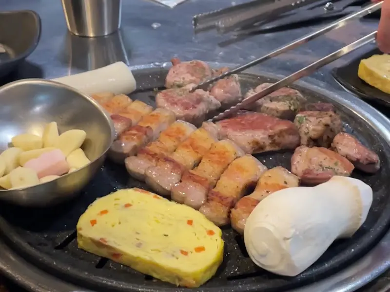 잘 구워진 오겹살 옆으로 마늘, 버섯, 계란찜이 가지런히 놓여 있다.