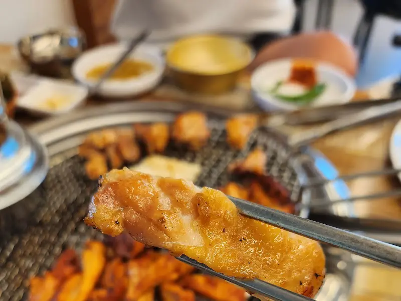 잘 구워진 닭갈비 한 점을 젓가락으로 집어 올린 모습