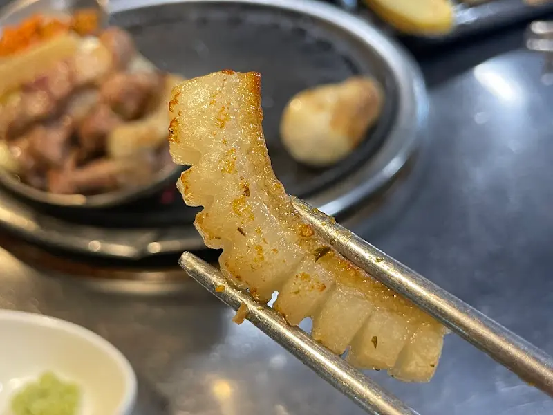 젓가락으로 집어 올린 잘 구워진 오겹살의 단면이 보인다. 