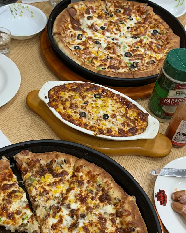 피자, 스파게티, 핫소스, 파마산 치즈가 테이블 위에 놓여 있다.