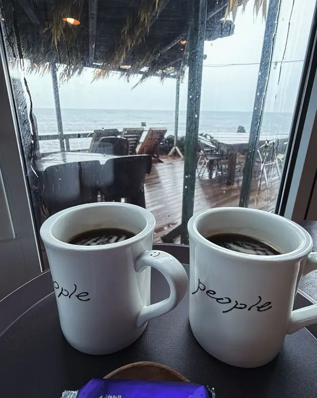 노을이 지는 바다를 바라보며 커피를 마시는 모습