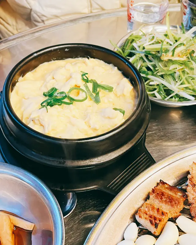 계란찜과 파채, 마늘, 쌈장 등이 놓여있는 테이블 사진