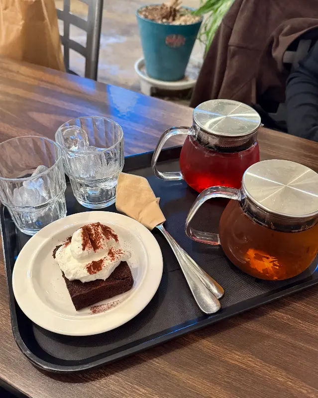 테이블 위에 놓인 차와 브라우니. 투명한 유리 주전자에 담긴 따뜻한 차와 크림이 올려진 브라우니가 정갈하게 놓여 있다.