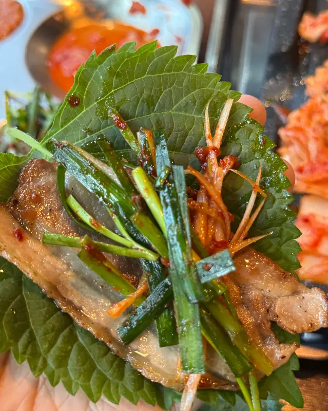 깻잎에 냉삼과 부추, 김치를 올려 쌈을 싼 모습